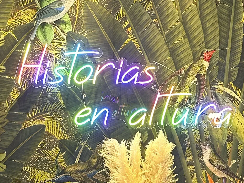 Rótulo de neón flex RGB «Historias en altura» sobre metacrilato en pared tropical